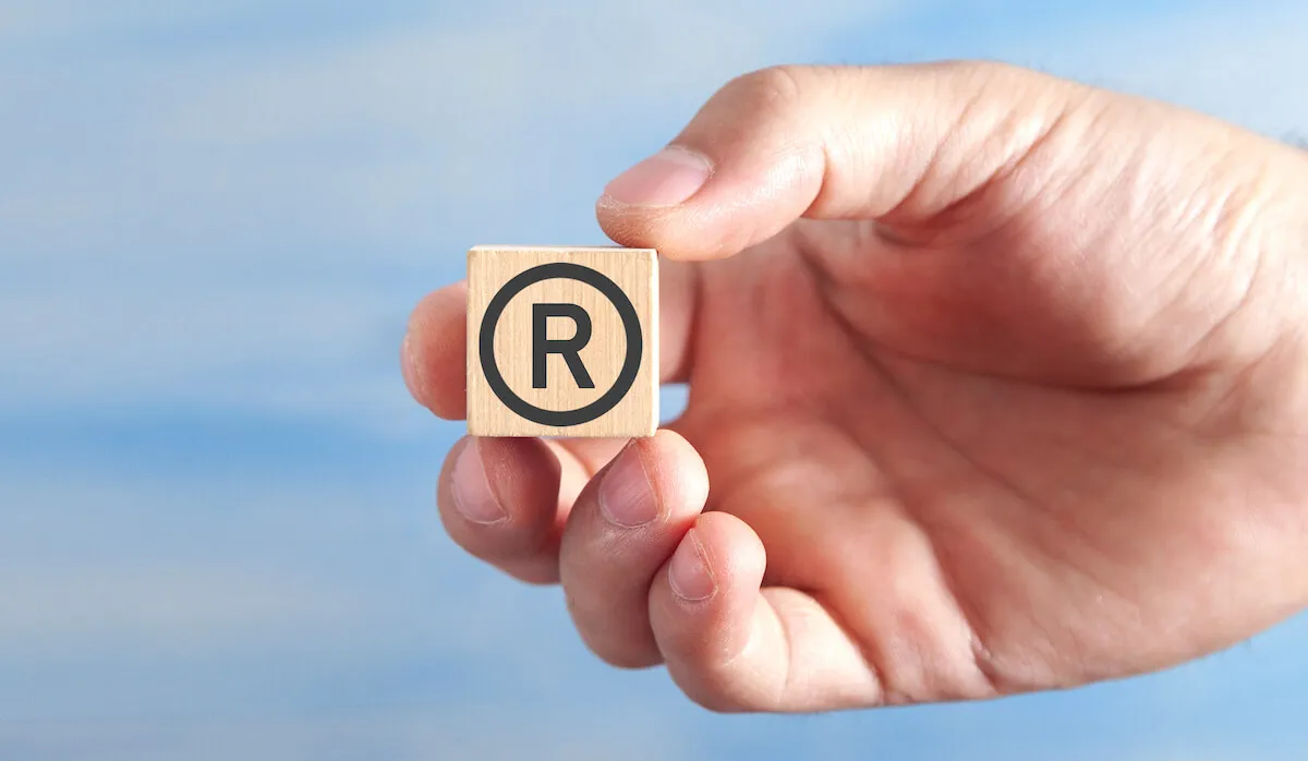 male hand showing rregistered trademark on wooden cube 1